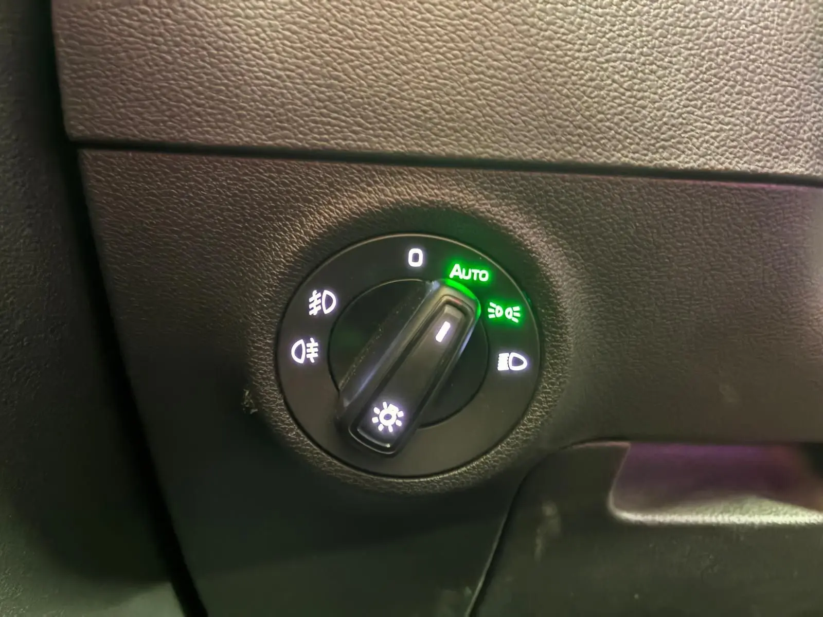 Gros plan sur le bouton de commande des phares du Skoda Karoq 2.0 TDI gris, avec mode automatique activé.