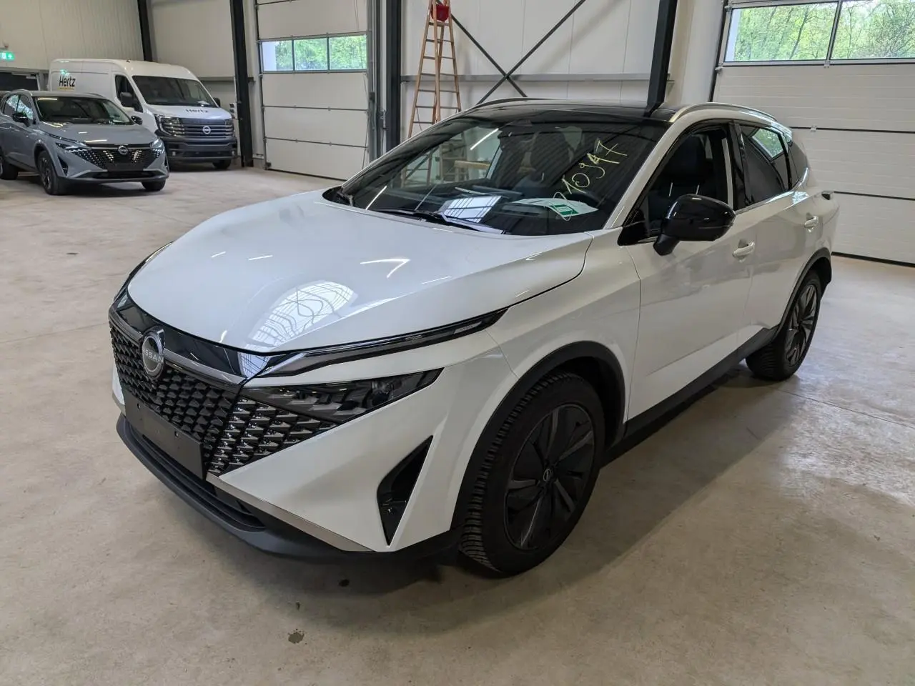 Nissan Qashqai blanc nacré en 3/4 avant droit, avec calandre noire et jantes alliage 19 pouces Aero.