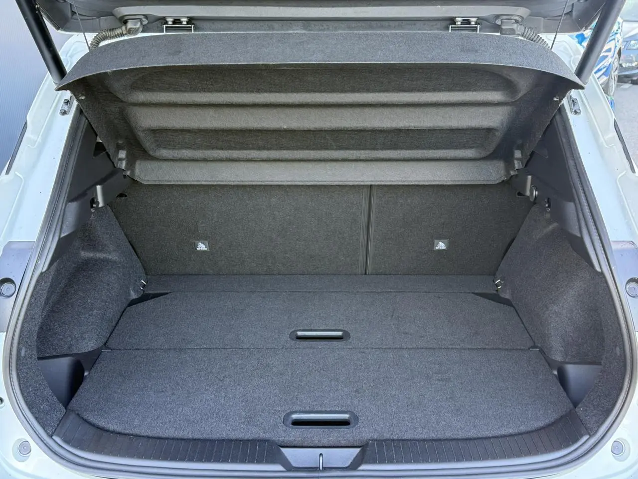 Coffre ouvert vu de l'arrière d'un Nissan Qashqai blanc nacré, espace de chargement plat et tapis gris.