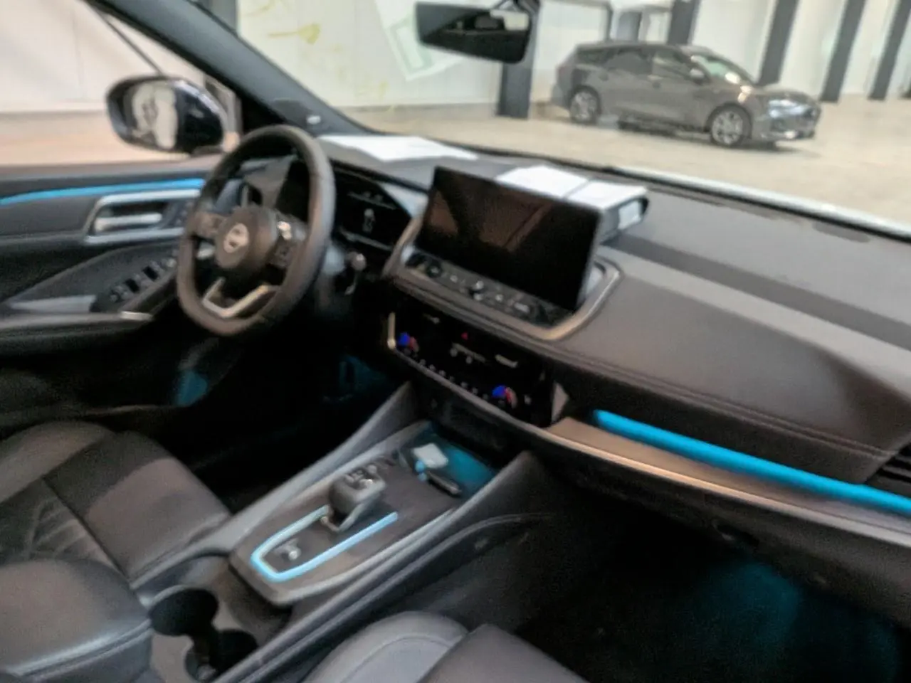 Vue intérieure côté conducteur du Nissan Qashqai 2025, sellerie noire avec éclairage d'ambiance bleu sur la console et tableau de bord.