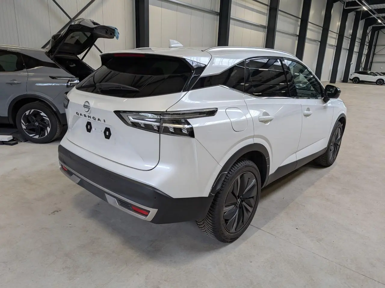 Vue 3/4 arrière droite du Nissan Qashqai blanc nacré avec toit noir et jantes alliage 19 pouces dans un garage.
