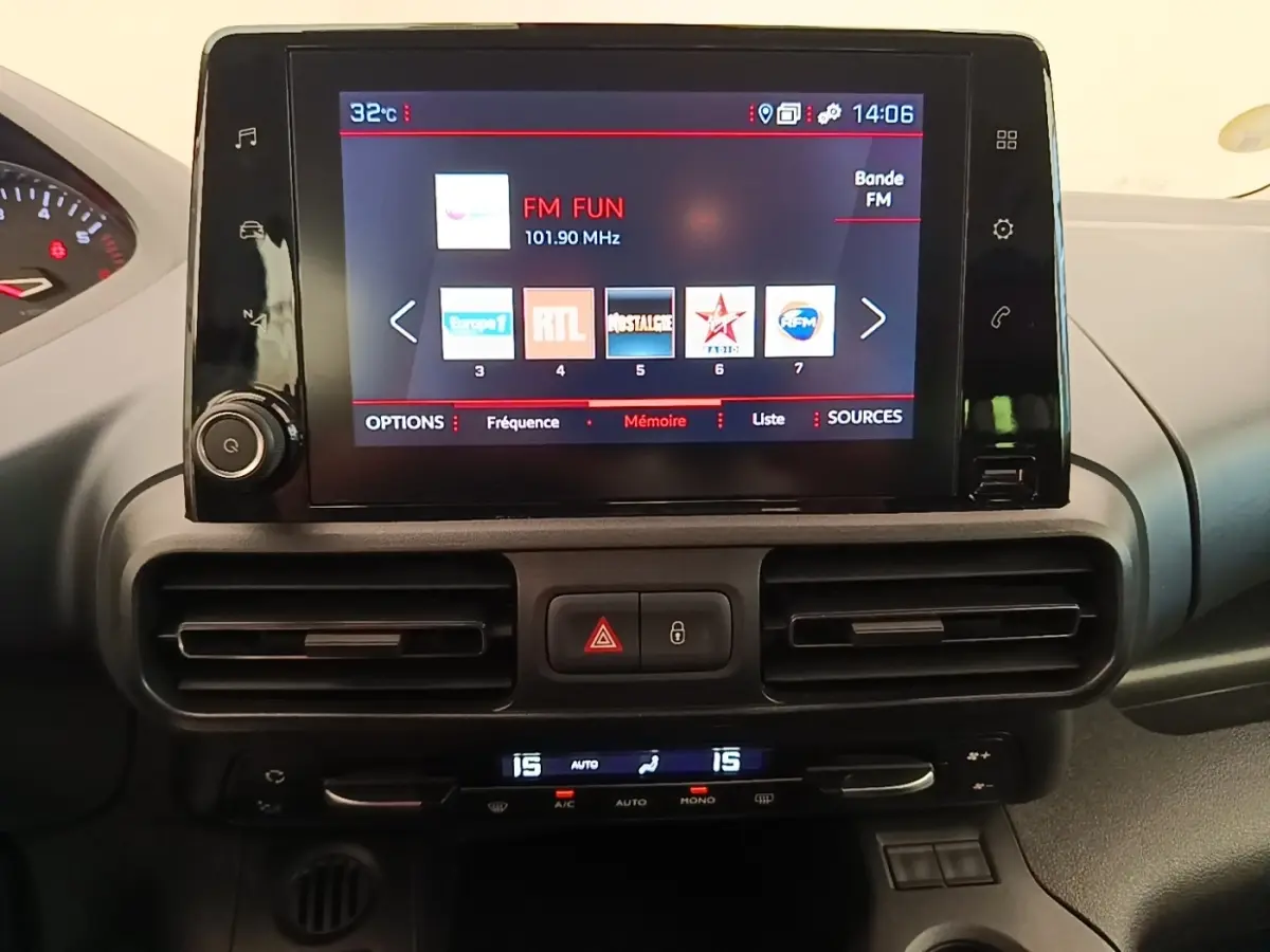 Écran tactile central allumé avec radio FM, tableau de bord noir du Peugeot Rifter blanc, vue intérieure frontale.