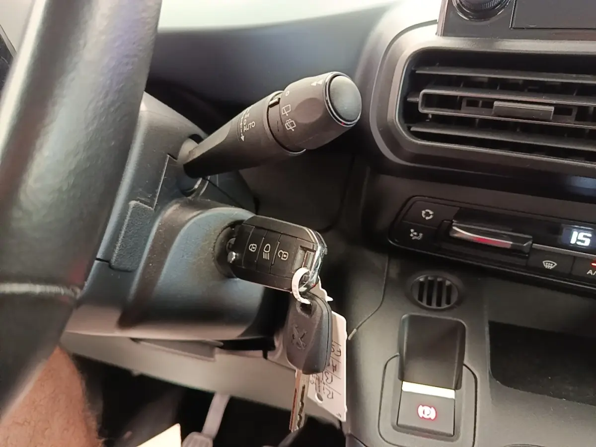Gros plan intérieur sur le volant cuir et clé insérée dans le contacteur d’un Peugeot Rifter 2020, tableau de bord noir visible.