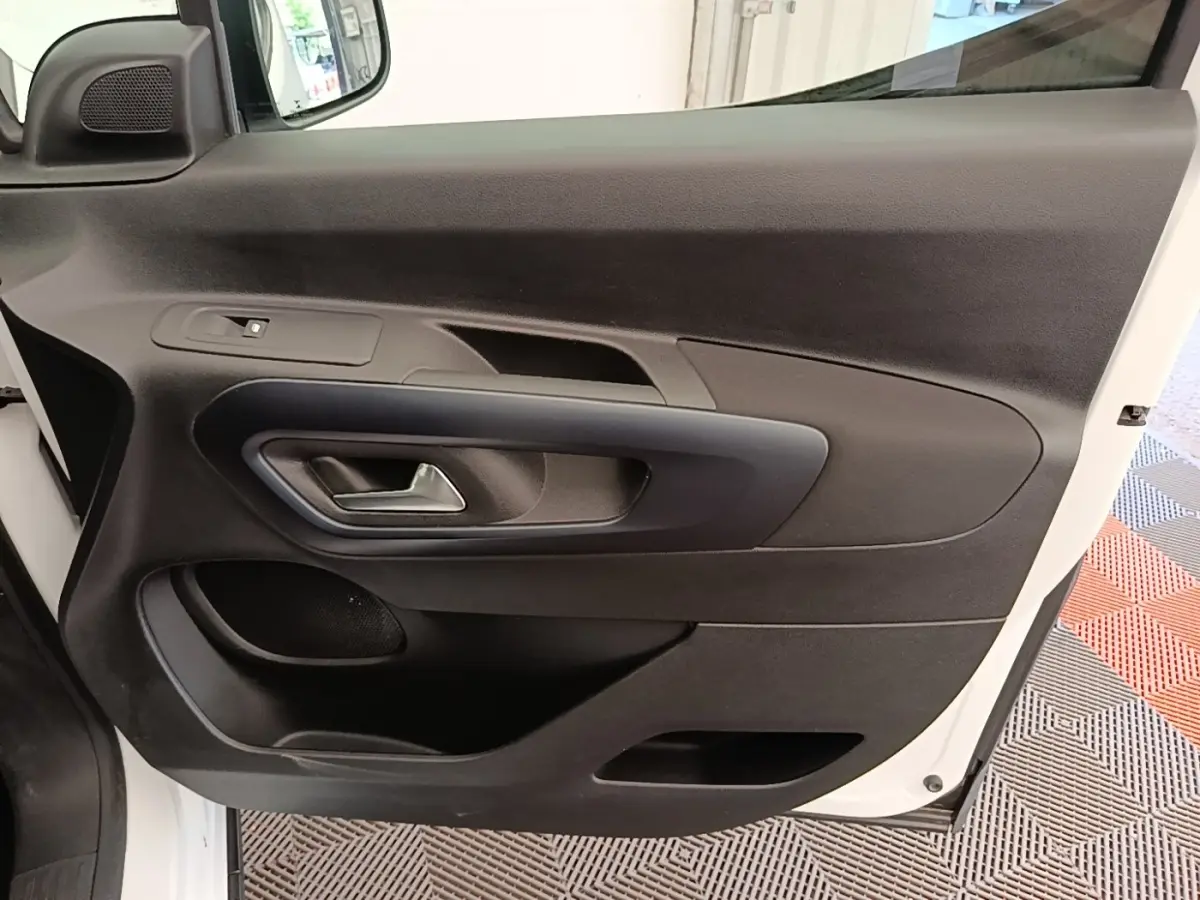 Vue rapprochée de la porte avant gauche noire du Peugeot Rifter blanc, montrant la poignée et les commandes de fenêtre.
