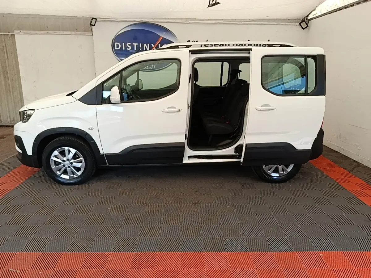 Vue de profil côté gauche d'un Peugeot Rifter blanc 2020 avec porte coulissante arrière ouverte, intérieur visible.
