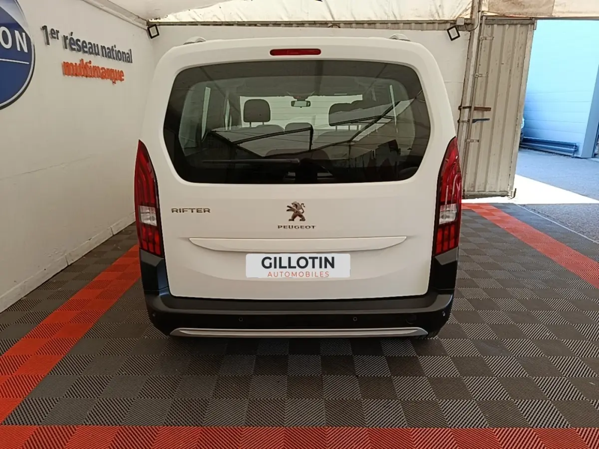 Vue arrière d'un Peugeot Rifter blanc 2020 avec feux arrière verticaux et pare-chocs noir dans un garage.
