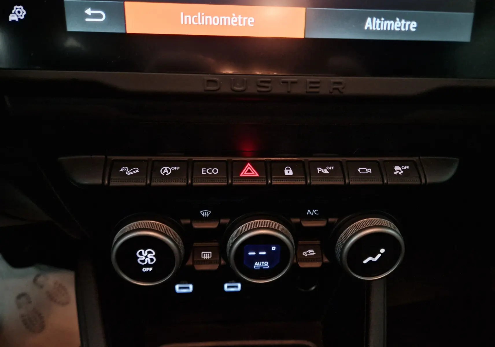 Détail du tableau de bord du Dacia Duster 2024 blanc montrant les commandes climatisation et boutons de fonctions assistées.