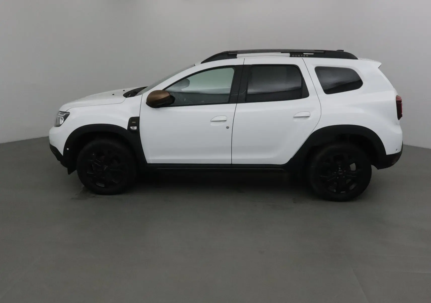Profil côté gauche d'un Dacia Duster blanc 2024 avec coques de rétroviseurs bronze et jantes noires.