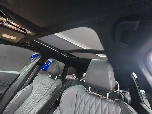 Intérieur BMW X1 M-Sport 2024 en cuir noir, vue depuis l'avant droit avec toit panoramique ouvrant visible.