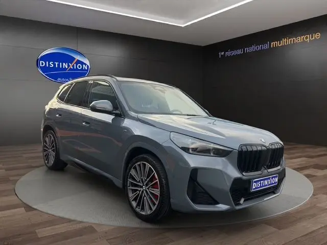BMW X1 Storm Bay en 3/4 avant droit, avec jantes alliage 20'' et freins M Sport rouges visibles en showroom