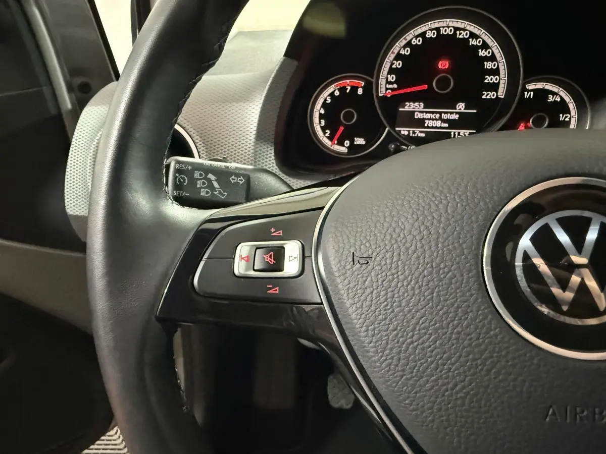 Gros plan sur le volant cuir multifonctions et le tableau de bord éclairé de la Volkswagen Up gris foncé 2022.