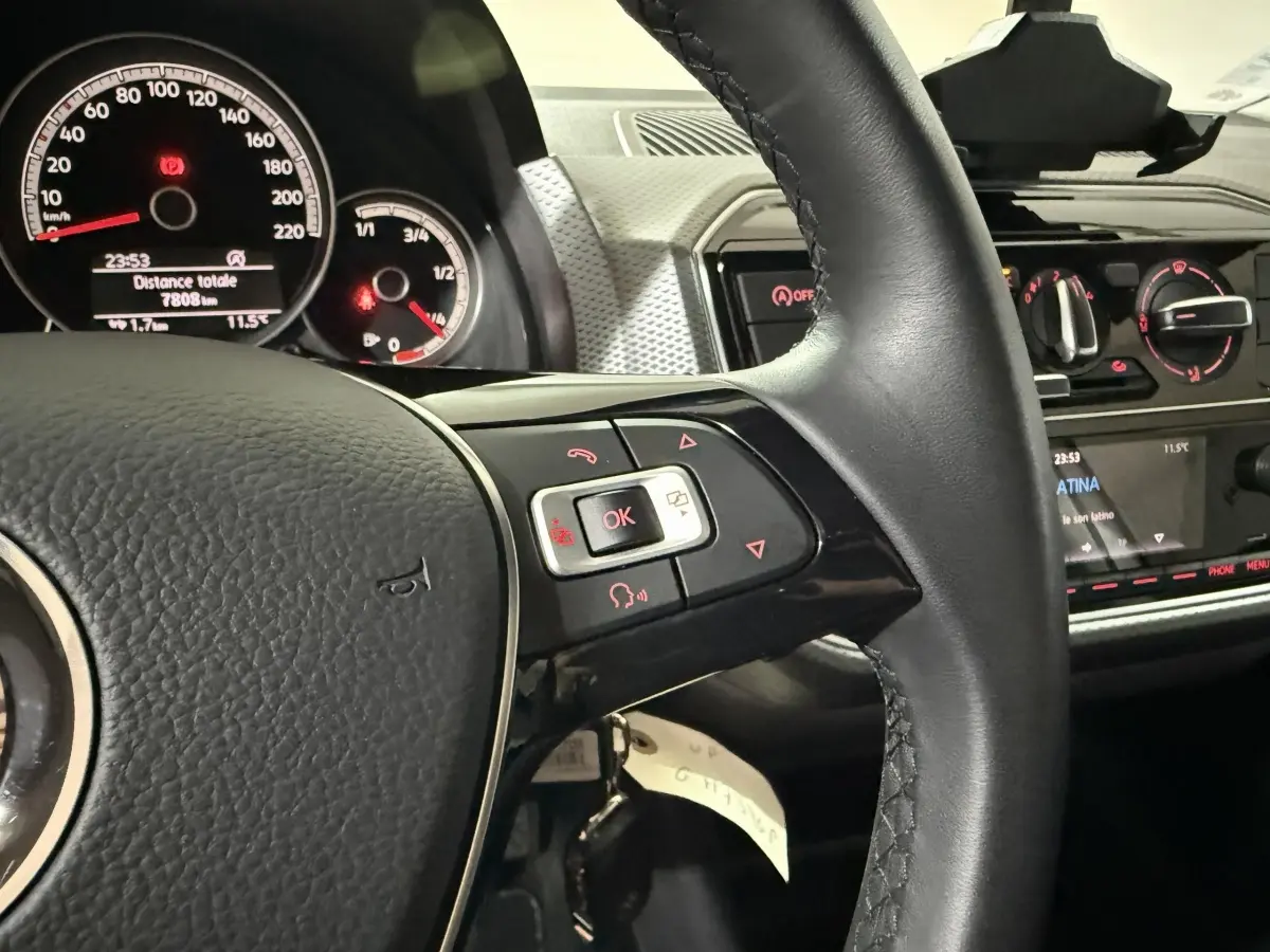 Gros plan sur le volant cuir et le tableau de bord du Volkswagen Up gris foncé, avec commandes multifonctions visibles.