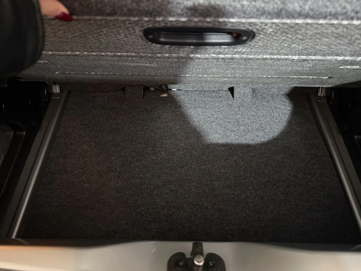 Coffre ouvert du Volkswagen Up gris foncé montrant le compartiment de rangement sous tablette.