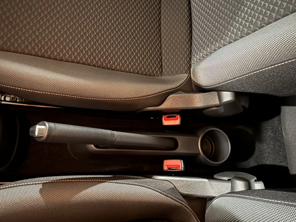 Vue rapprochée de la console centrale du Volkswagen Up gris foncé 2022, avec frein à main manuel et sièges en tissu.