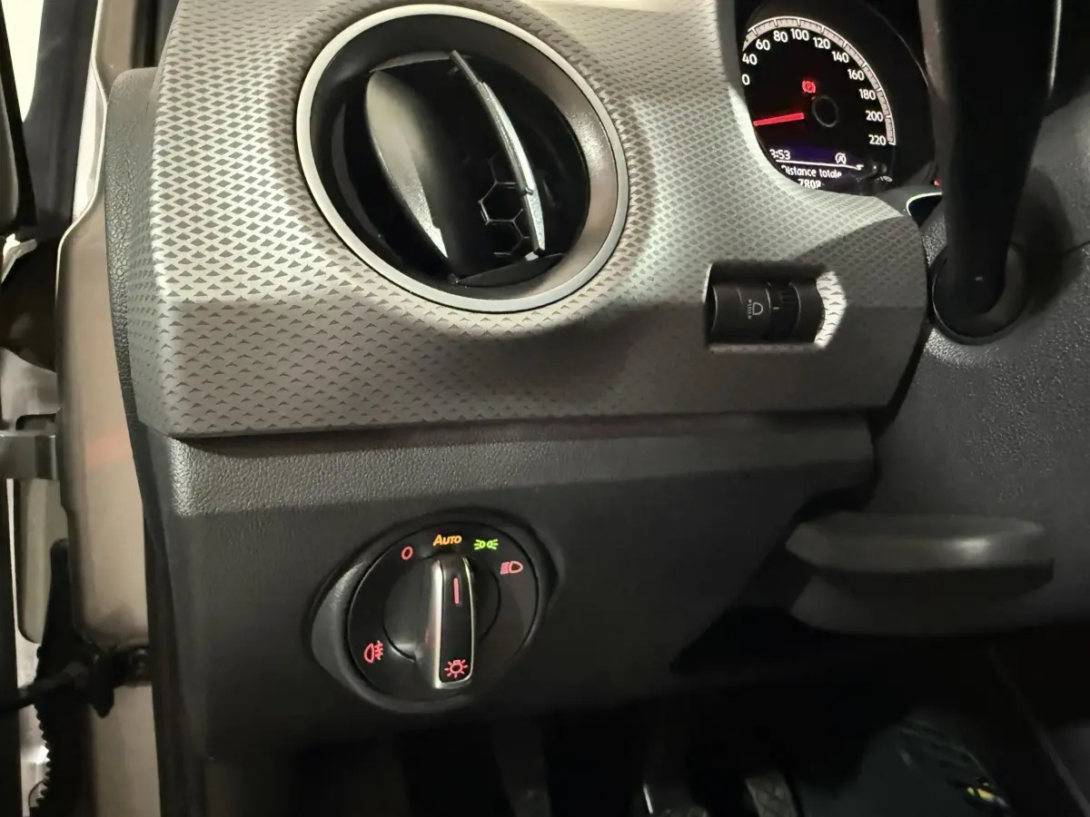 Détail du tableau de bord gris avec commande des phares et aérateur rond dans une Volkswagen Up 2022 vue côté gauche.