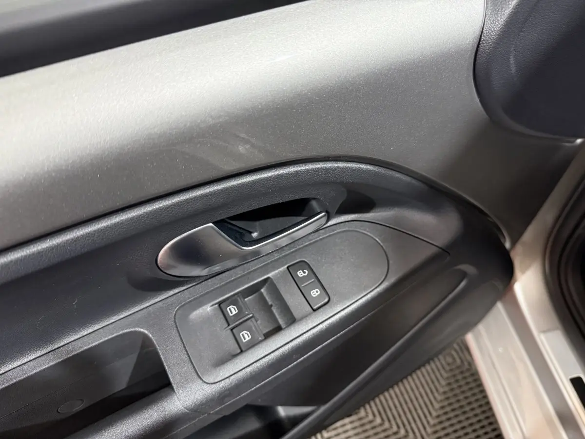 Poignée intérieure et commandes de vitres côté conducteur d'une Volkswagen Up gris foncé, vue rapprochée.