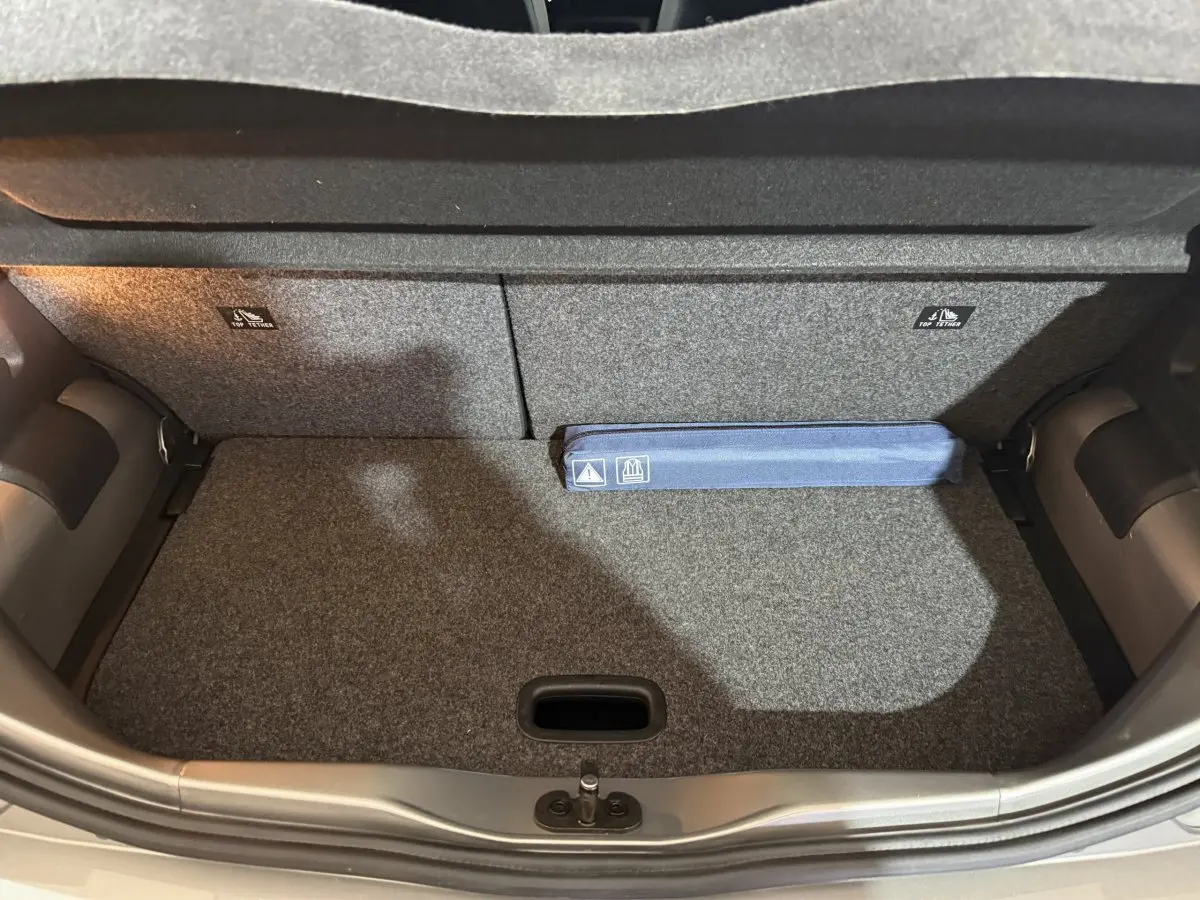 Coffre ouvert de la Volkswagen Up 1.0 65 Active gris foncé, montrant la moquette et un kit de sécurité bleu.