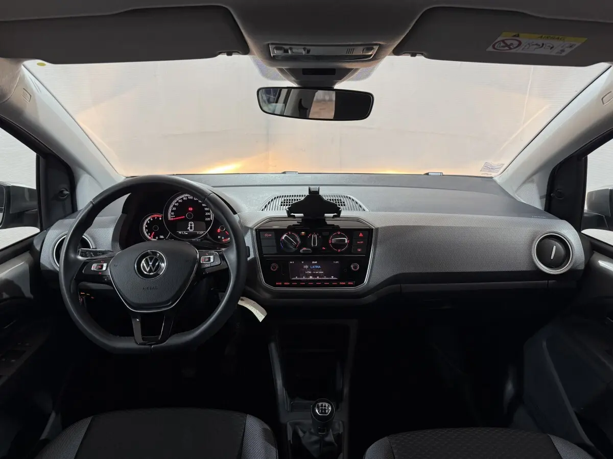 Vue frontale de l'intérieur du Volkswagen Up gris foncé 2022, volant cuir, tableau de bord avec écran et boîte manuelle.