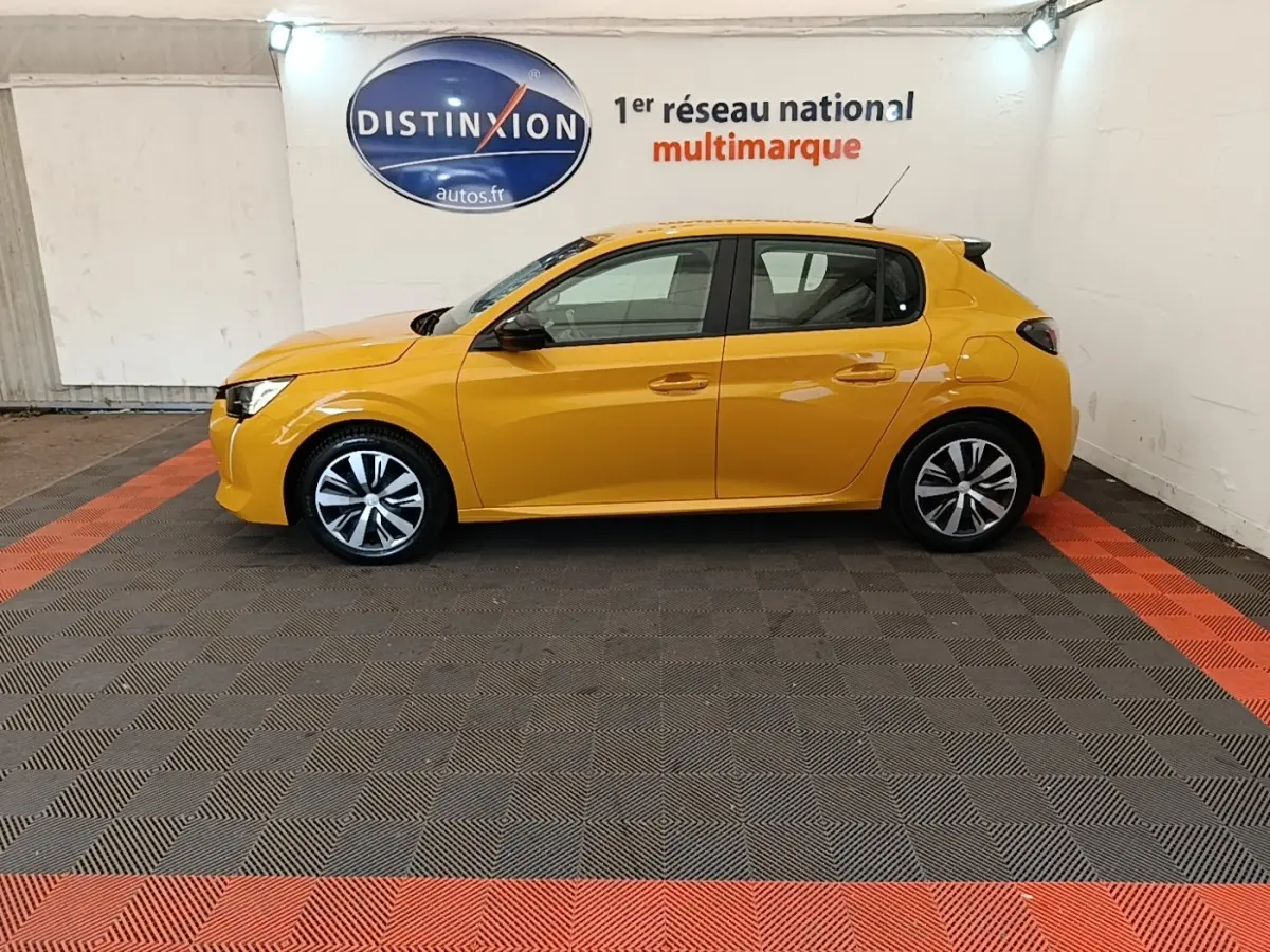 Peugeot 208 jaune vue de profil côté gauche dans un showroom avec sol gris et bandes rouges.