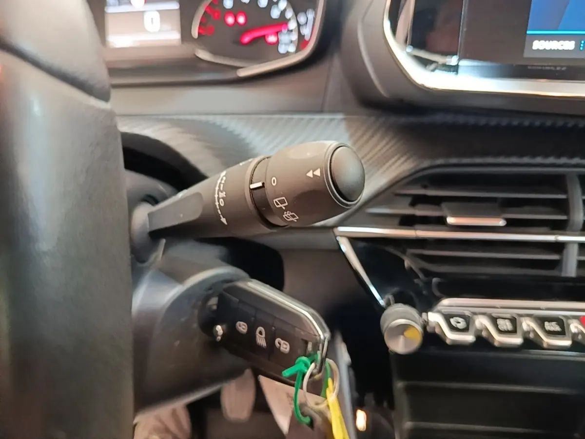 Gros plan sur la colonne de direction et le volant cuir de la Peugeot 208, avec tableau de bord et commandes visibles.