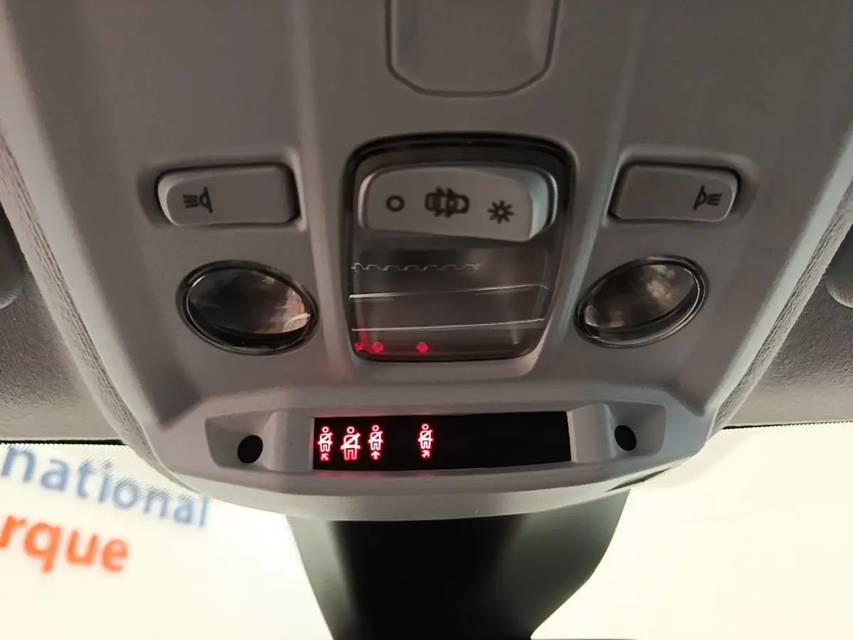 Vue rapprochée du plafonnier intérieur de la Peugeot 208 jaune, avec commandes d'éclairage et voyants de ceinture allumés.