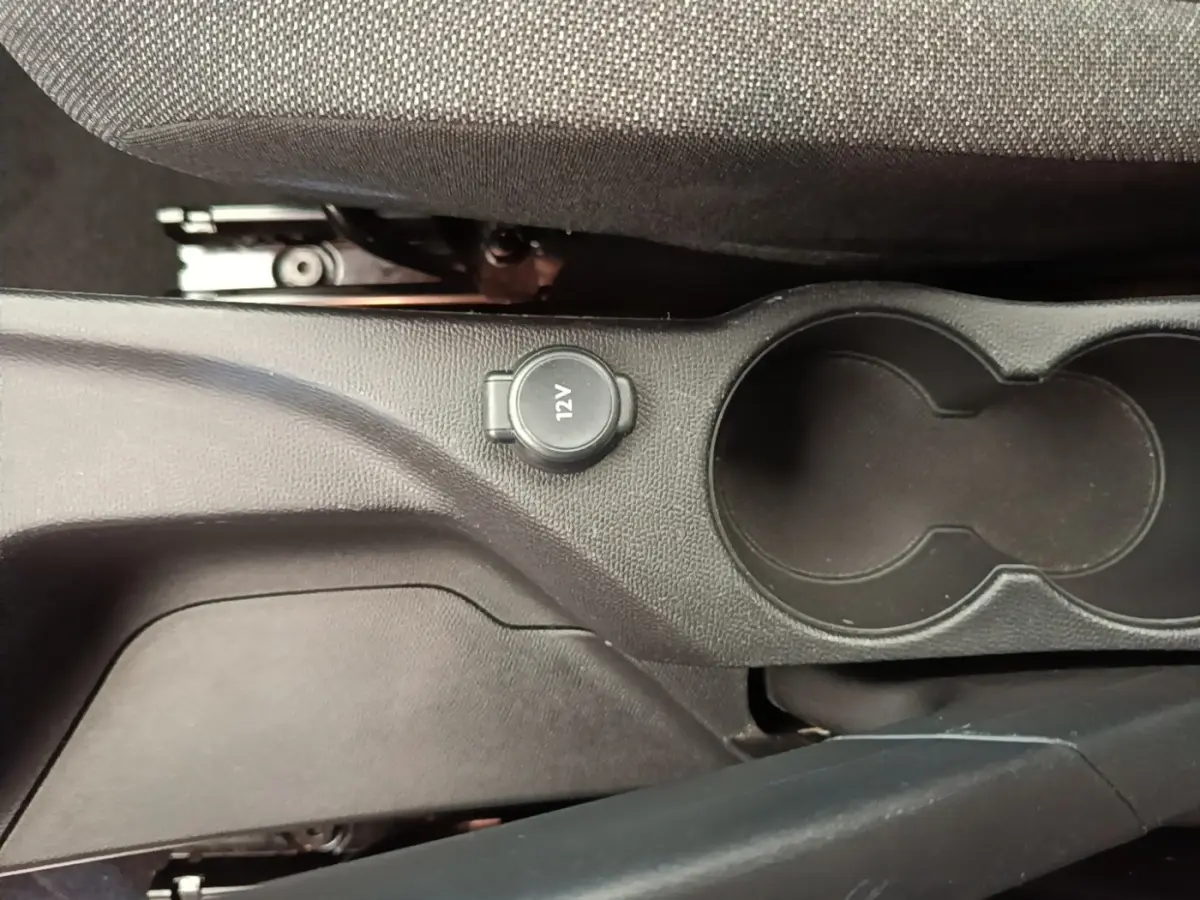 Vue rapprochée de la console centrale noire de la Peugeot 208 avec prise 12V et porte-gobelets.
