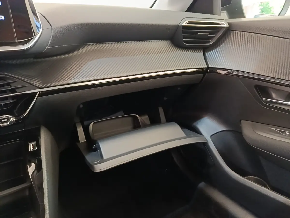 Intérieur de la Peugeot 208 PureTech 75 S&S Active Pack 2023, vue côté passager avec boîte à gants ouverte et tableau de bord noir texturé.