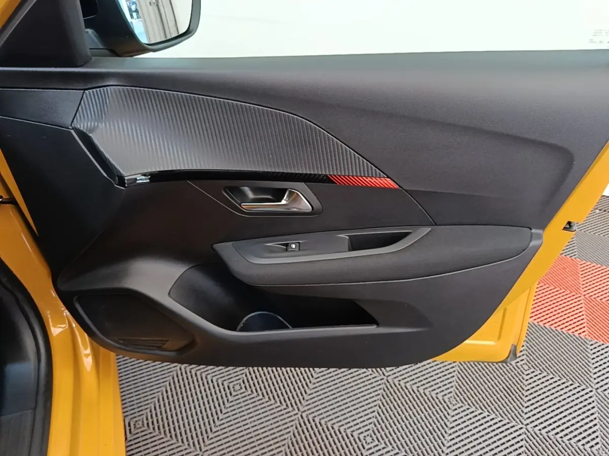 Vue latérale de la porte avant gauche noire avec insert effet carbone et bande rouge sur Peugeot 208 jaune 2023.
