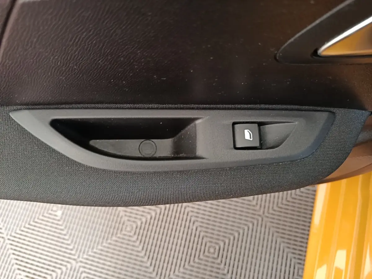 Détail de la commande de lève-vitre côté conducteur sur porte intérieure noire d’une Peugeot 208 jaune.