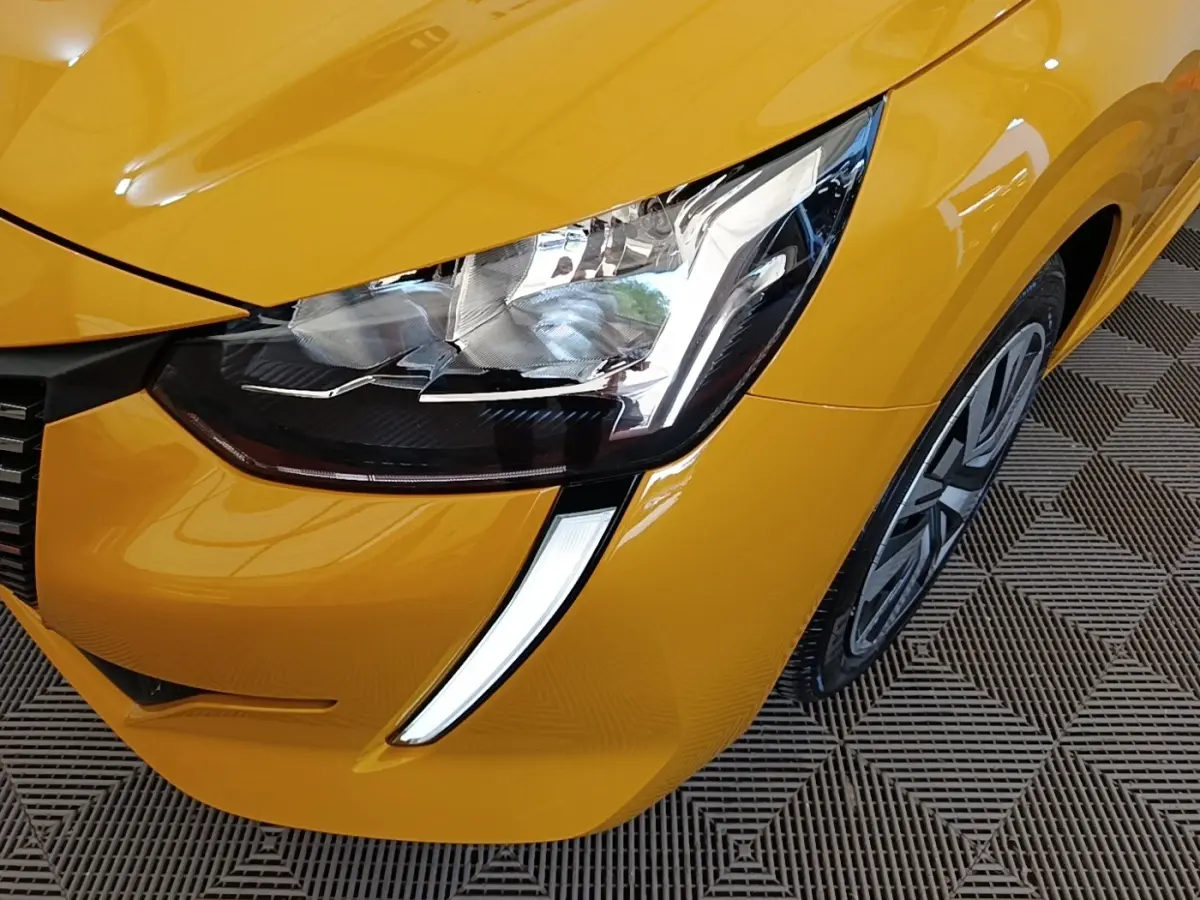 Gros plan sur le phare avant droit et la calandre d'une Peugeot 208 jaune vif, avec feux LED en forme de griffes.