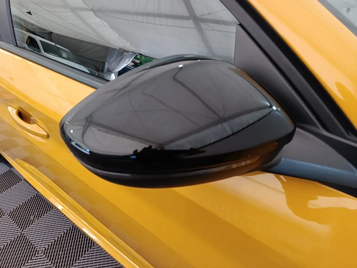 Rétroviseur extérieur noir côté gauche d'une Peugeot 208 jaune vue en gros plan sur fond intérieur.
