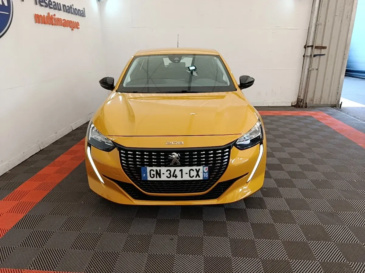 Peugeot 208 jaune vue de face en intérieur, avec calandre noire et feux LED en forme de griffes.
