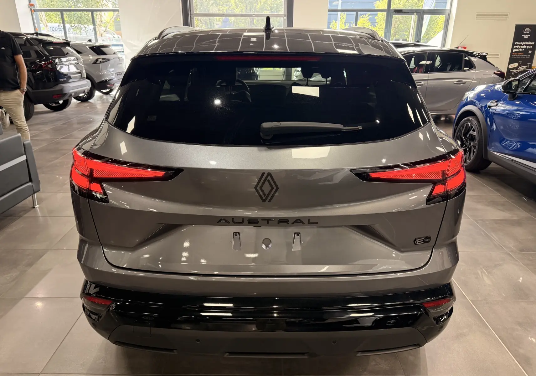 Vue arrière d'un Renault Austral gris schiste avec toit noir, feux LED allumés, en showroom lumineux.