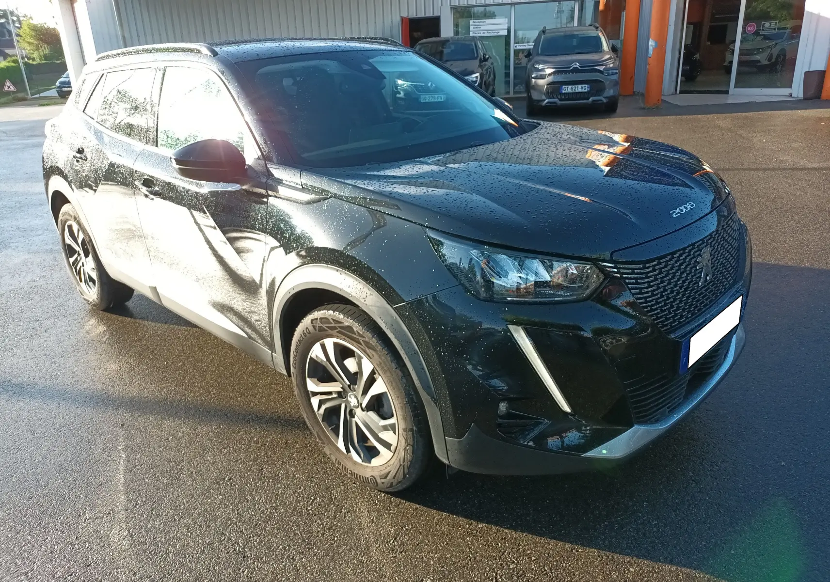 Peugeot 2008 noir vue 3/4 avant droit, carrosserie brillante avec gouttes d'eau et jantes alliage bicolores.