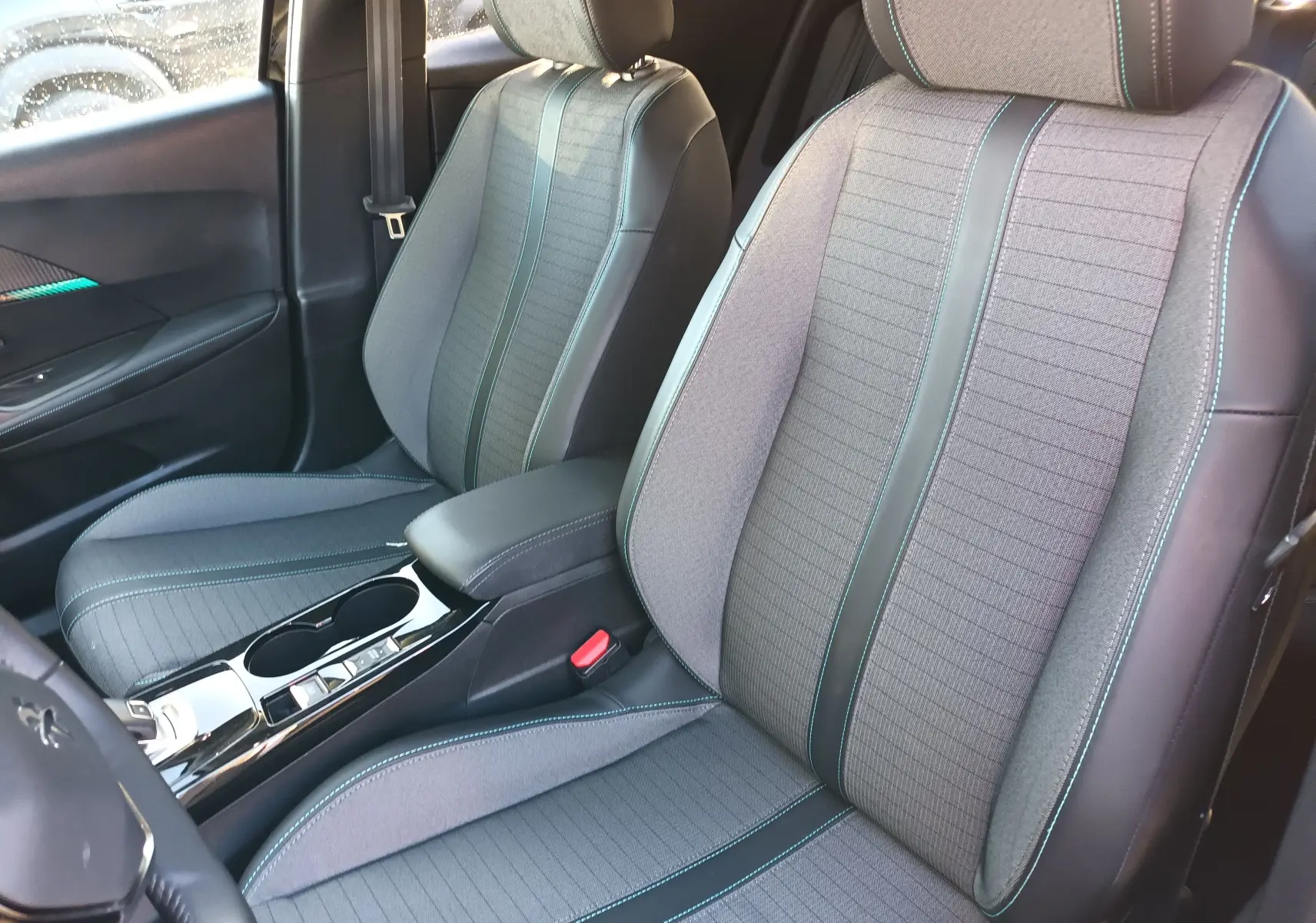 Intérieur avant du Peugeot 2008 noir 2022, sièges en tissu gris avec surpiqûres bleues et console centrale brillante.