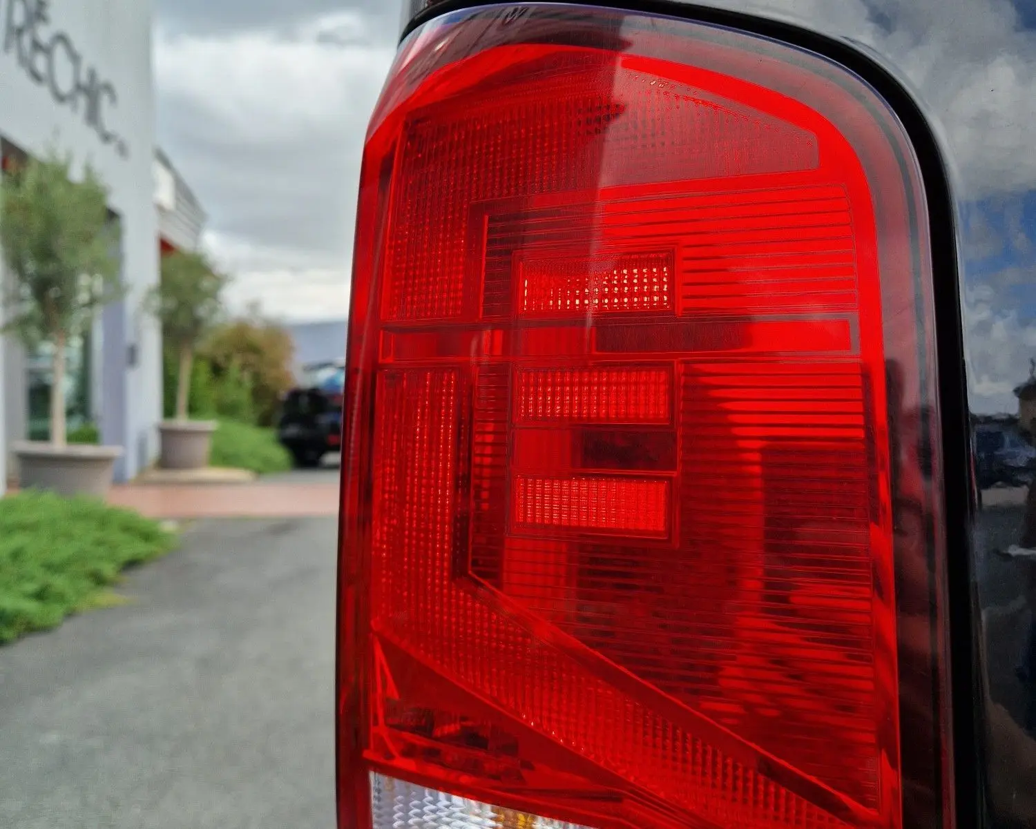 Gros plan sur le feu arrière droit rouge du Volkswagen Transporter noir, reflétant le ciel et un bâtiment en arrière-plan.