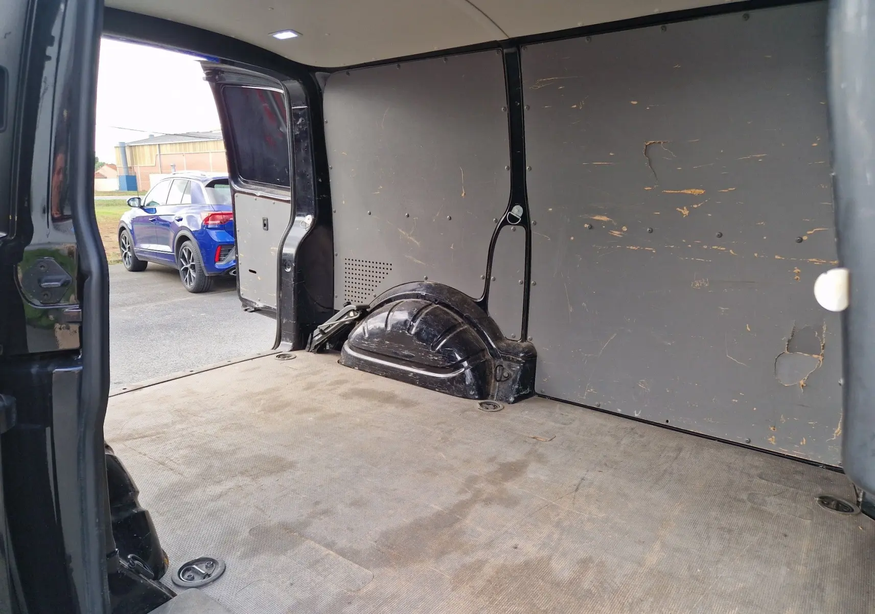 Vue intérieure arrière du Volkswagen Transporter noir 2020, montrant l'espace de chargement avec plancher universel usé.