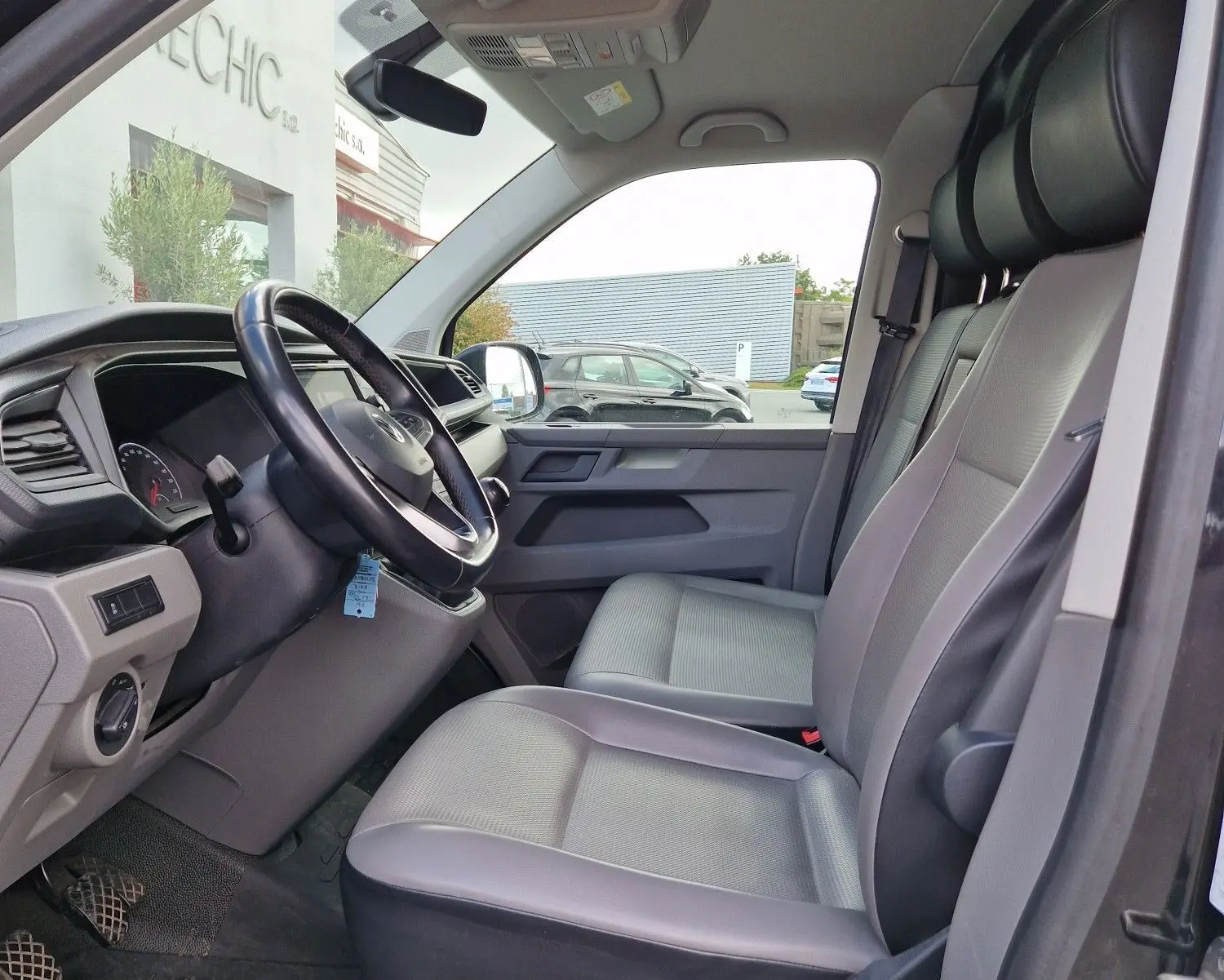 Vue intérieure côté conducteur du Volkswagen Transporter noir 2020, montrant le volant multifonction et les sièges avant gris.