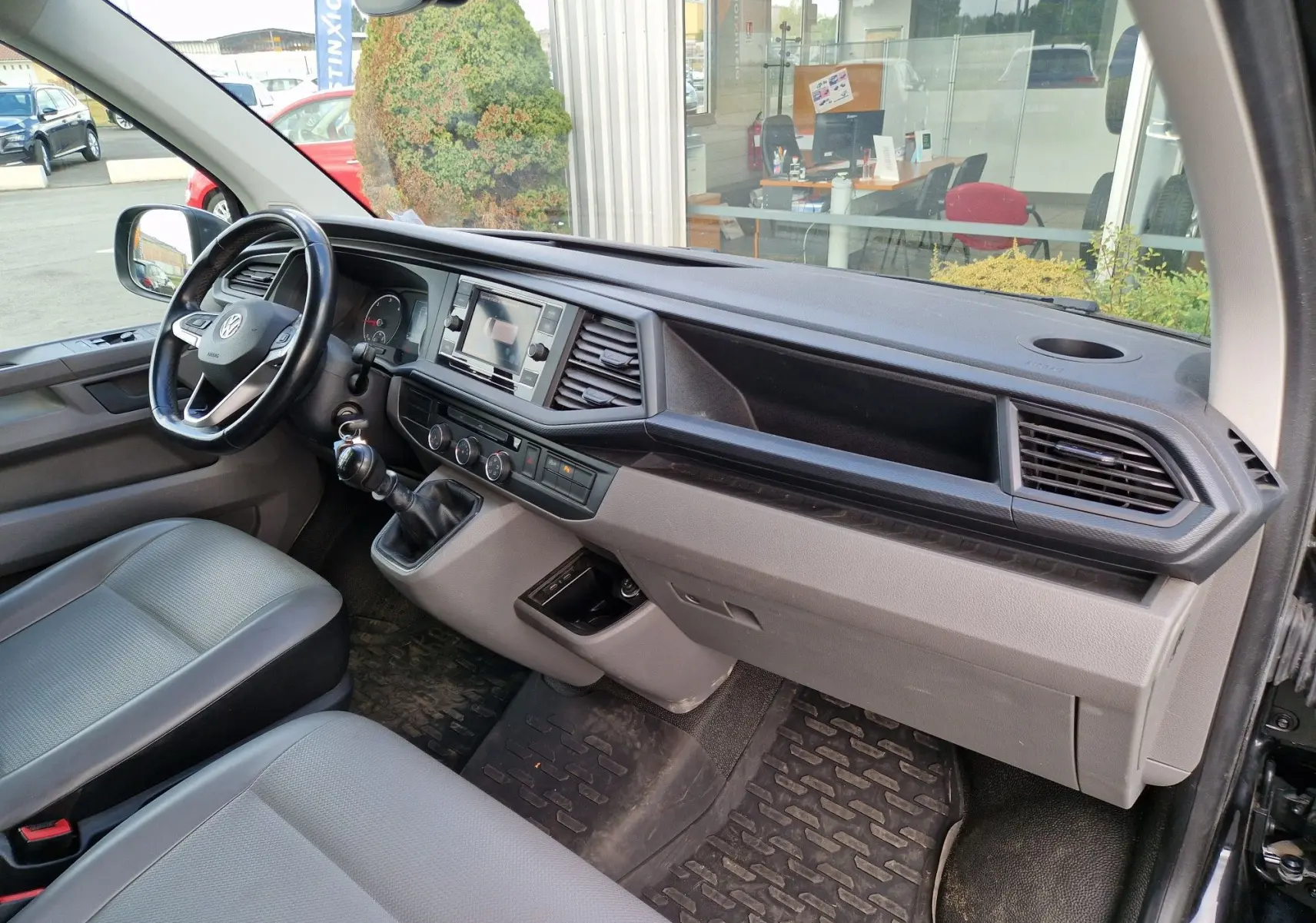 Vue intérieure côté conducteur du Volkswagen Transporter noir 2020, avec tableau de bord moderne et boîte manuelle.