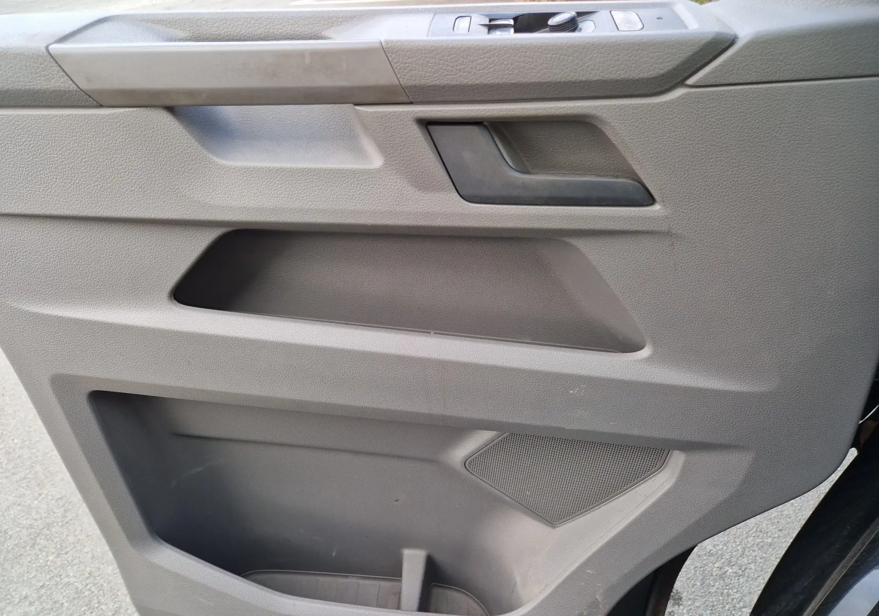 Gros plan sur la porte côté droit du Volkswagen Transporter noir, montrant la poignée, les rangements et l'haut-parleur intégré.