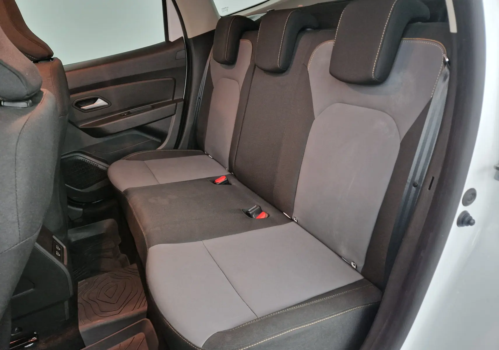 Vue latérale droite de la banquette arrière grise et noire du Dacia Duster 2024 blanc, avec appuie-têtes et ceintures visibles.