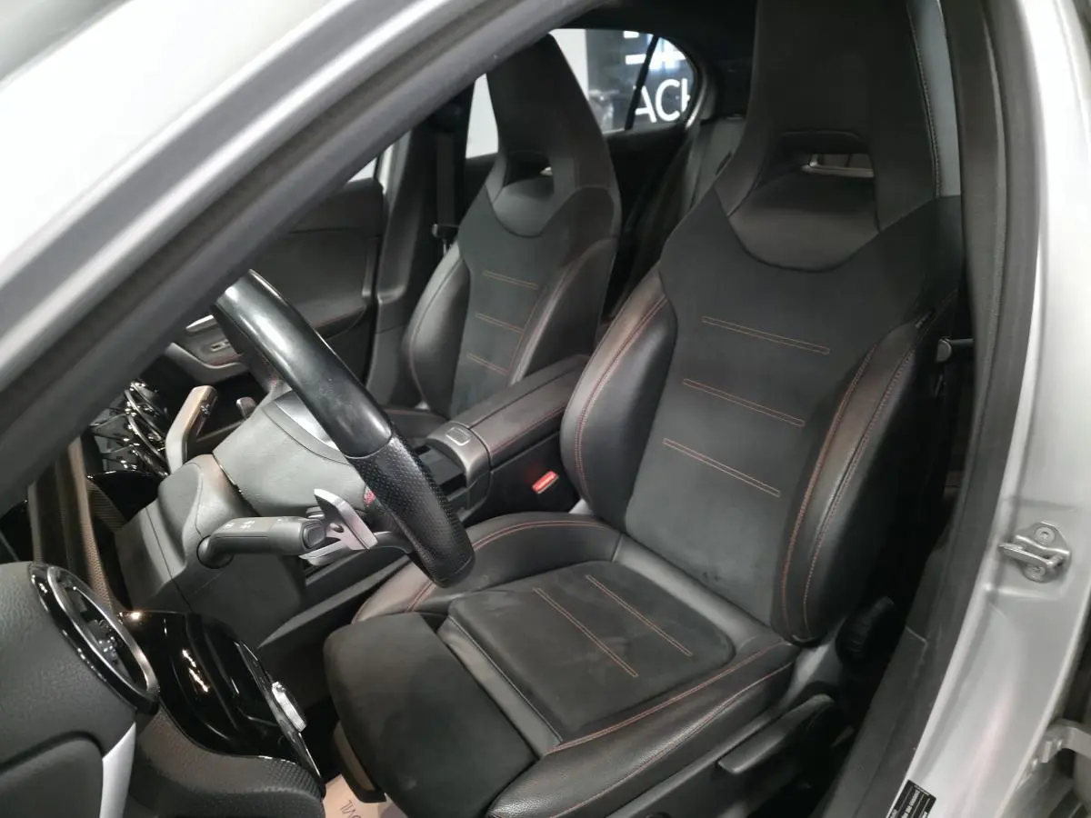 Intérieur côté conducteur d'une Mercedes Classe A gris, sièges sport noirs avec surpiqûres rouges visibles.
