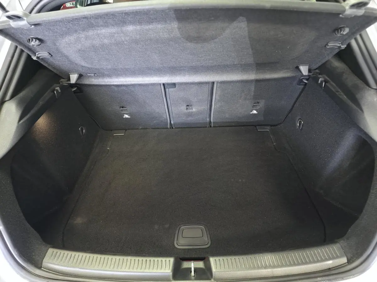 Coffre ouvert vu de l'arrière d'une Mercedes Classe A AMG Line gris, espace de chargement vide et tapis noir.