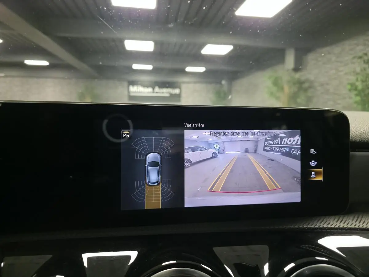 Affichage de la caméra de recul sur l'écran central d'une Mercedes Classe A gris, vue arrière avec lignes de guidage jaunes.