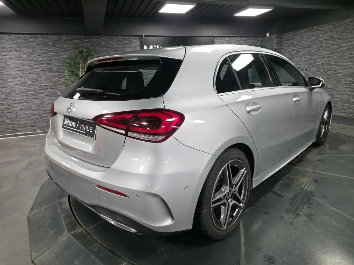Vue 3/4 arrière droite d'une Mercedes Classe A gris métallisé avec jantes AMG et feux arrière LED dans un showroom.