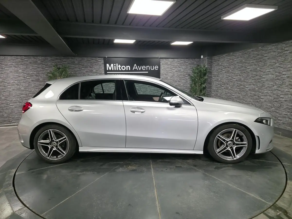 Profil côté gauche d'une Mercedes Classe A gris métallisé AMG Line avec jantes alliage cinq branches dans un showroom.