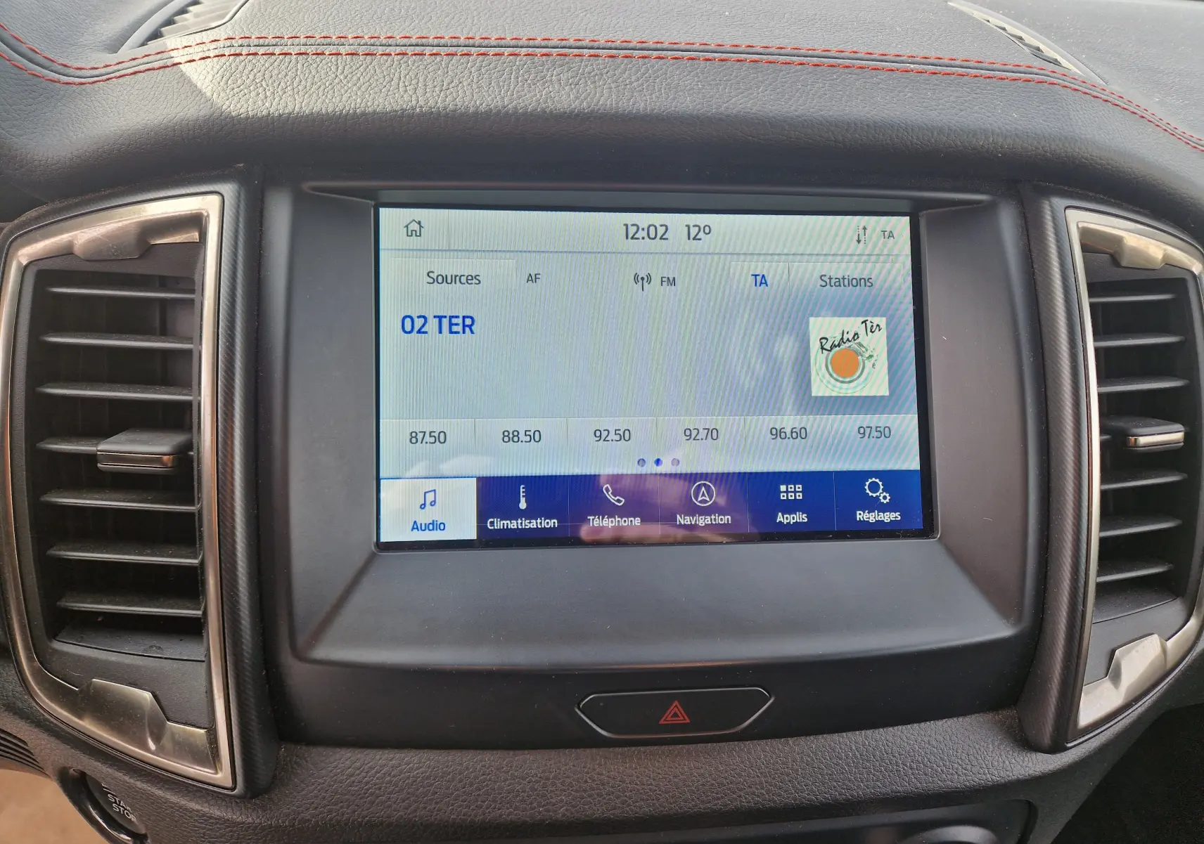 Écran tactile central du Ford Ranger Raptor 2022 avec affichage radio, entouré de garnitures noires et coutures rouges sur le tableau de bord.