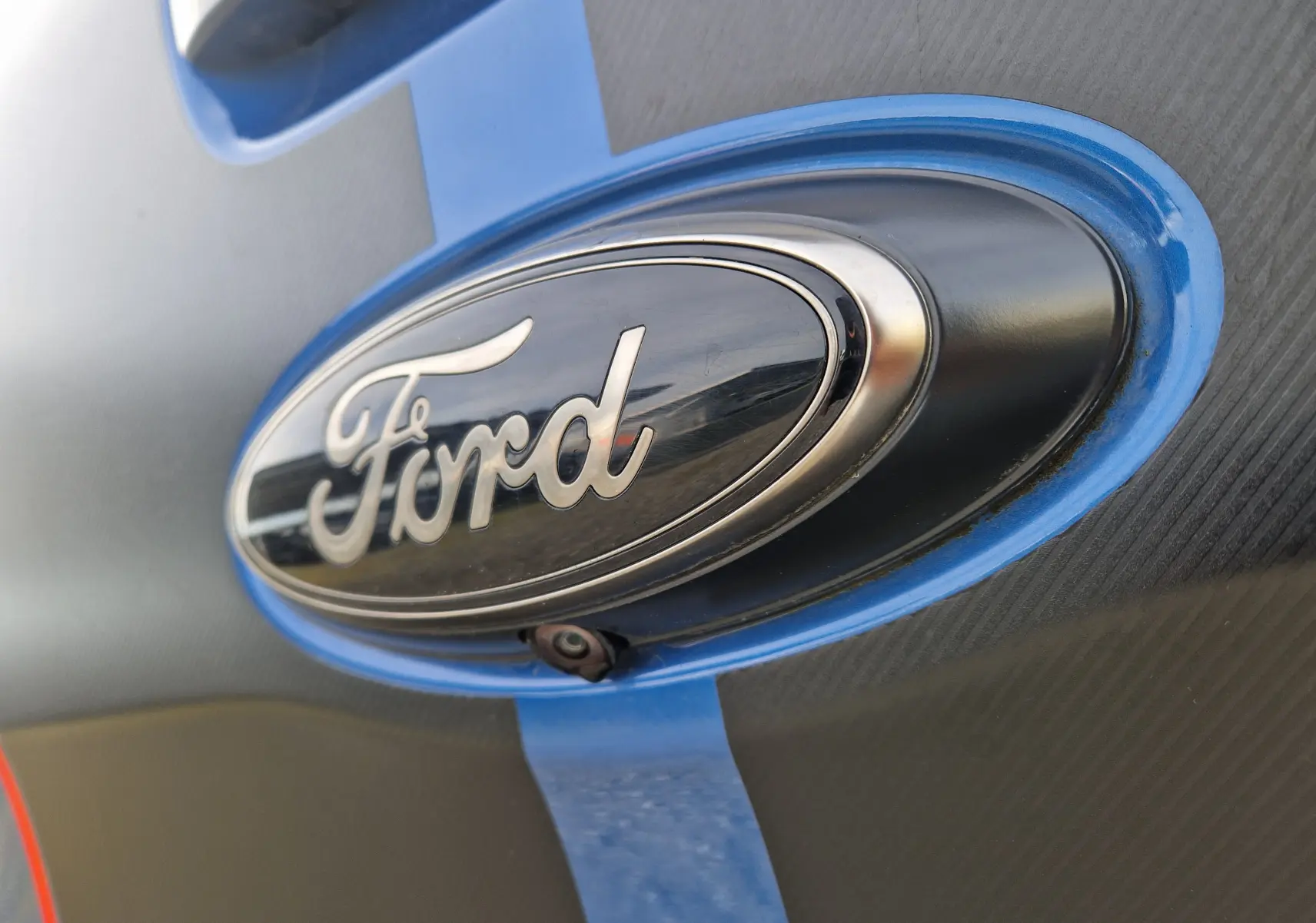 Gros plan sur l'emblème Ford noir et argent entouré d'un liseré bleu Ford Performance sur la carrosserie grise.