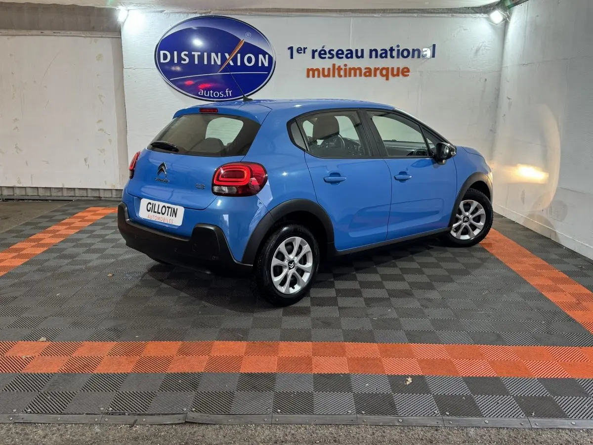 Citroën C3 bleu en 3/4 arrière droit dans un showroom avec logo Distinxion en arrière-plan.