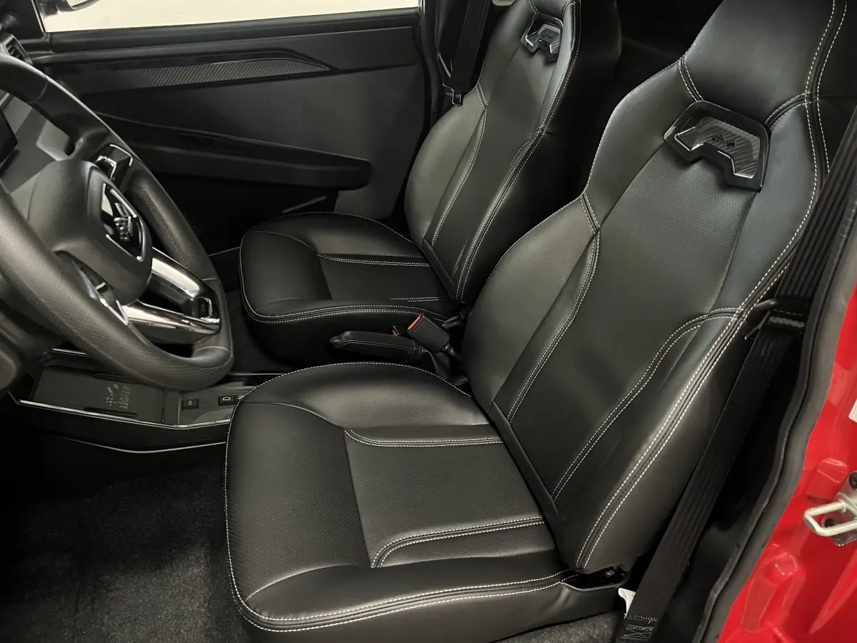 Vue intérieure côté conducteur montrant les sièges noirs en cuir avec surpiqûres blanches et partie de la portière rouge.